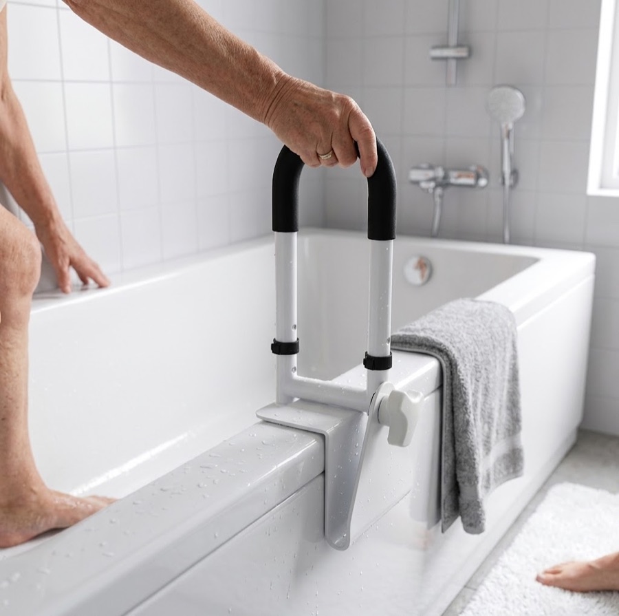 An older person's hand grips a clamp-on rail on the rim of a white bathtub while stepping in.