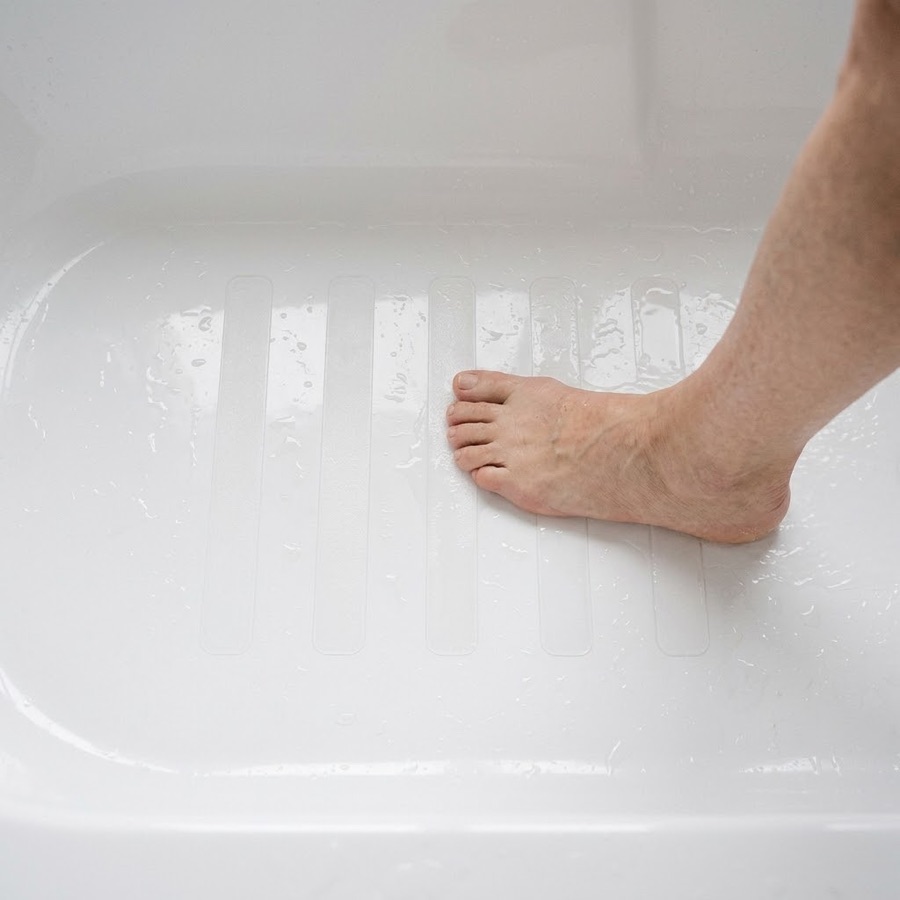 A bare foot steps onto clear non-slip strips across the wet floor of a white bathtub.